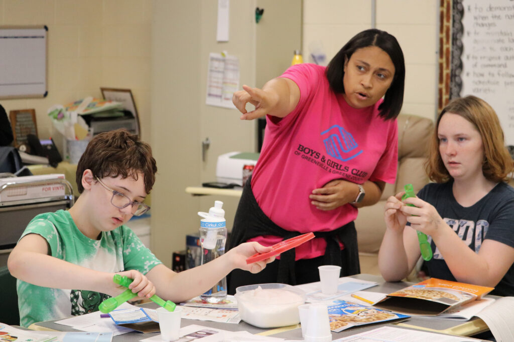 Boys and Girls club leader pointing while at table with two kids