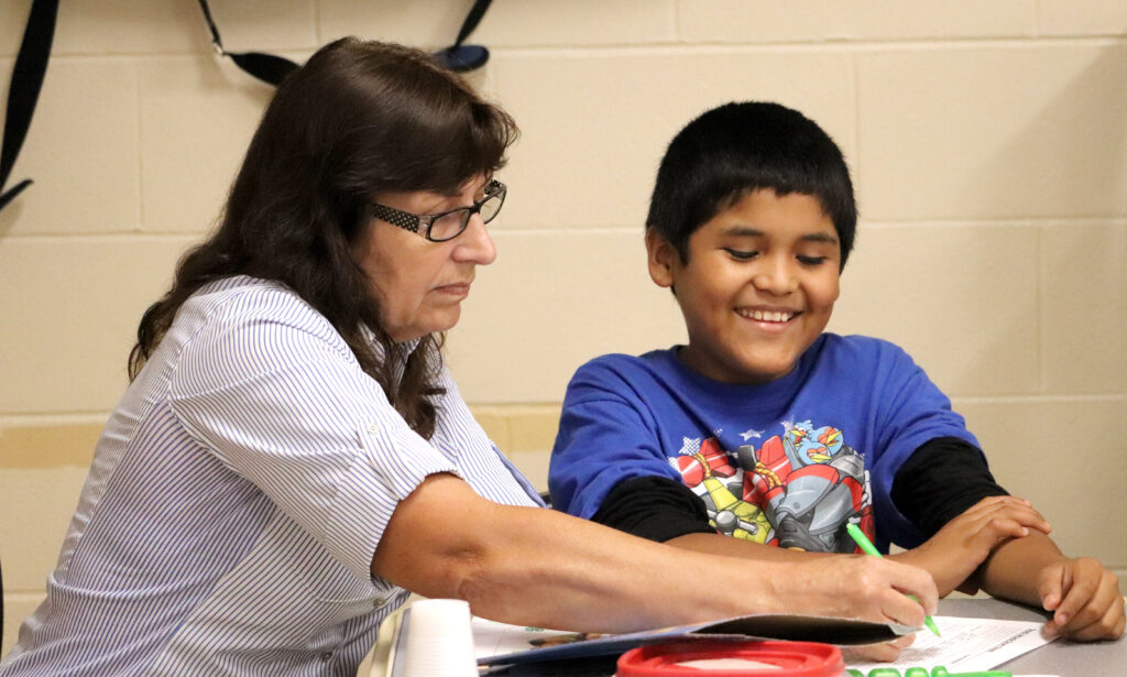 teacher and student working on worksheet at table while smiling